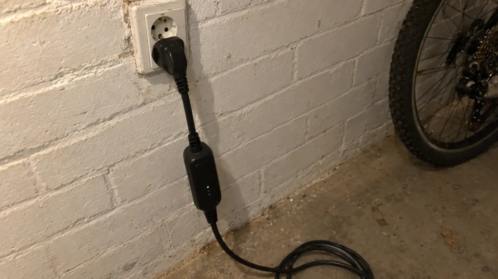 Cable de carga portátil de coche eléctrico enchufado a una toma de corriente doméstica en la pared de ladrillo de un garaje