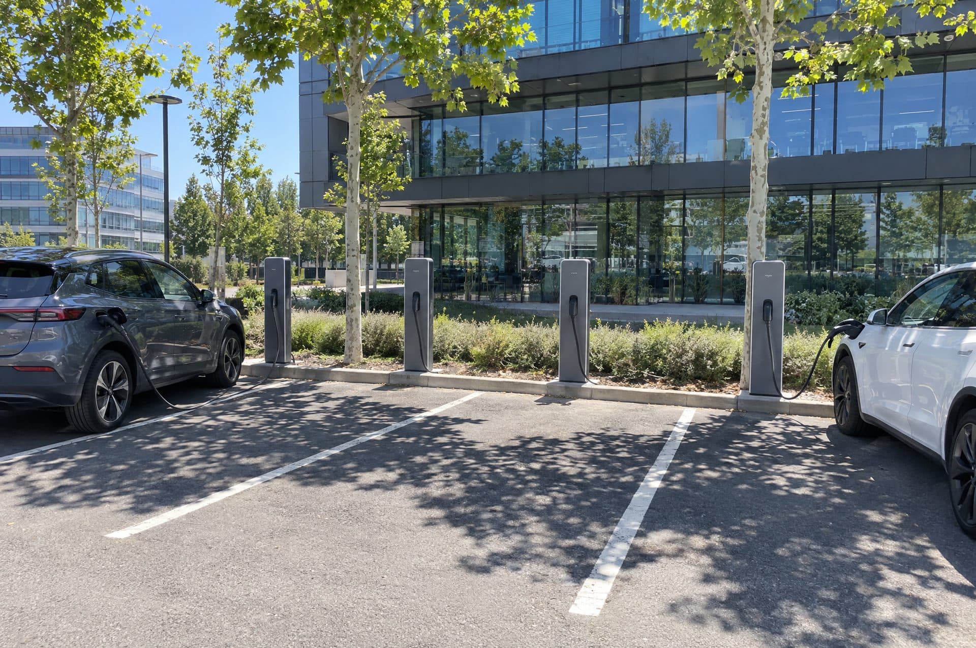 Aparcamiento de un edificio de oficinas con cuatro postes de recarga entre plazas y dos coches de empresa cargando