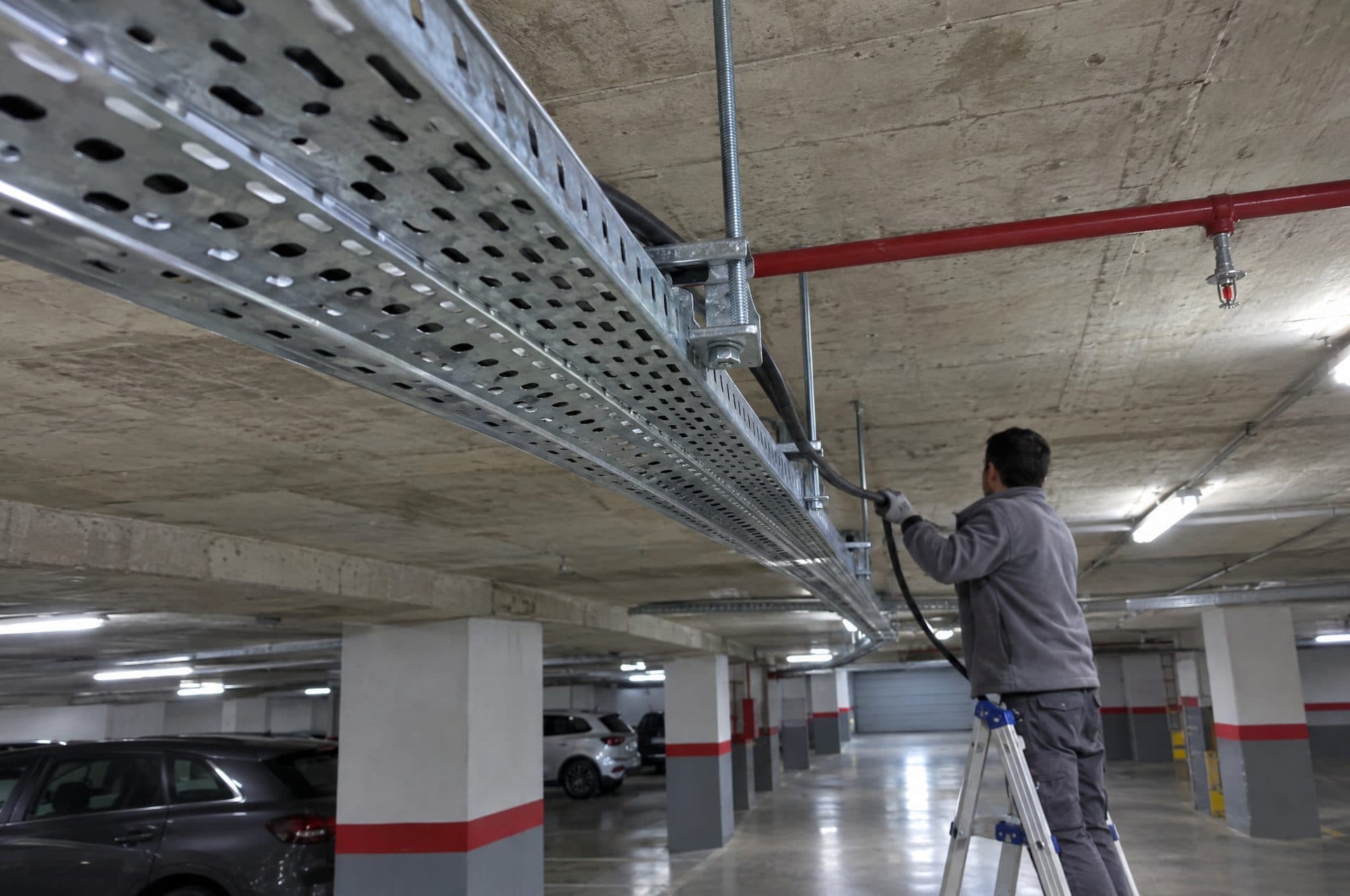 Bandeja portacables galvanizada colgada del techo de un garaje mientras un electricista tira de un cable desde una escalera