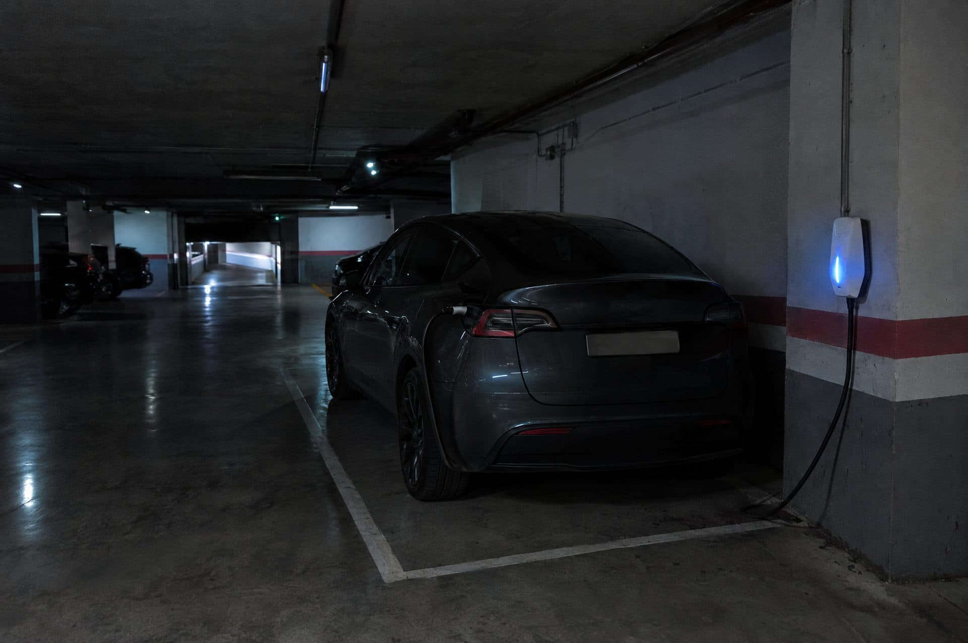 Coche eléctrico cargando de noche en un garaje en penumbra, con el piloto azul del cargador encendido