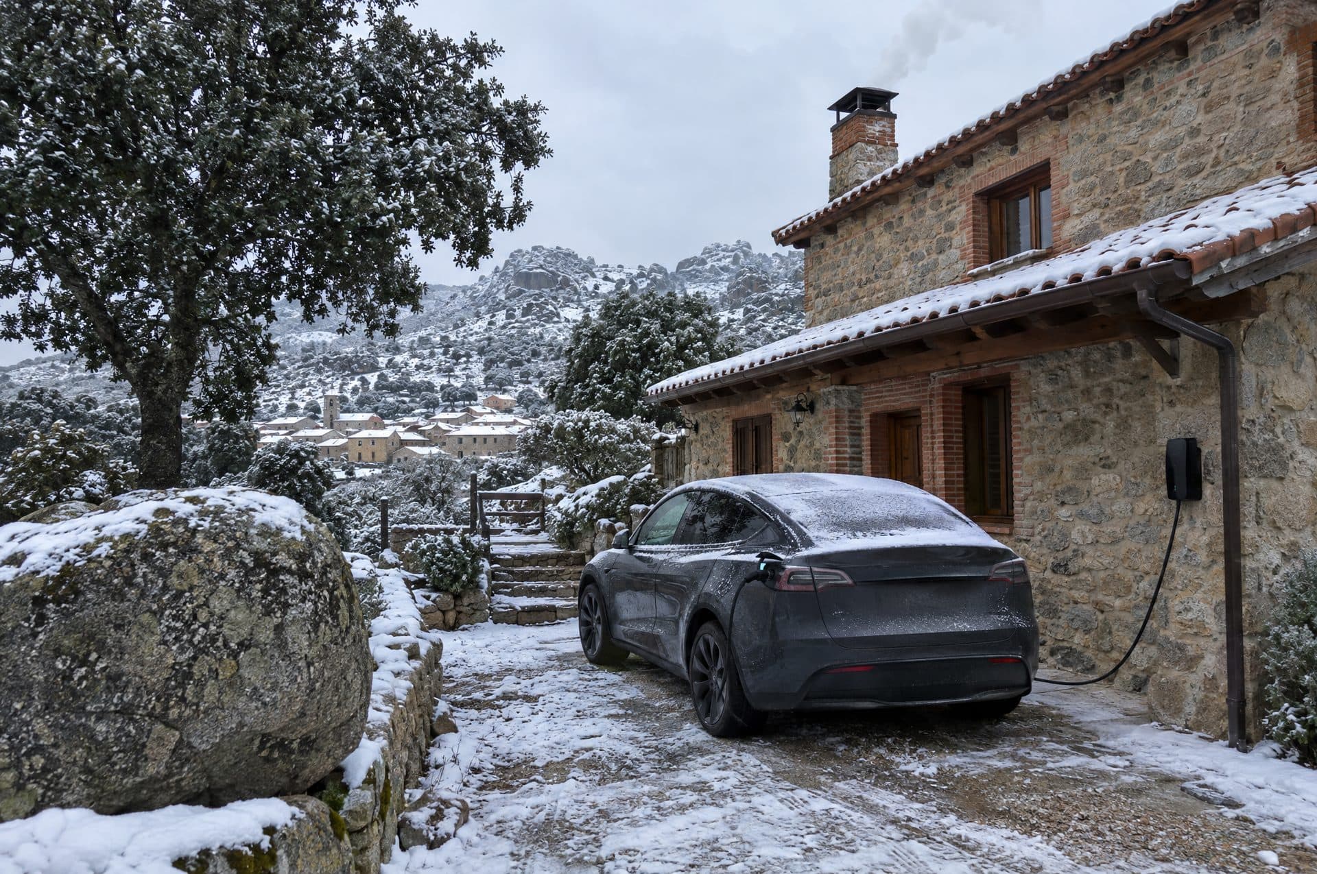 Casa de piedra en un pueblo de sierra nevado con un coche eléctrico cargando en el camino de entrada