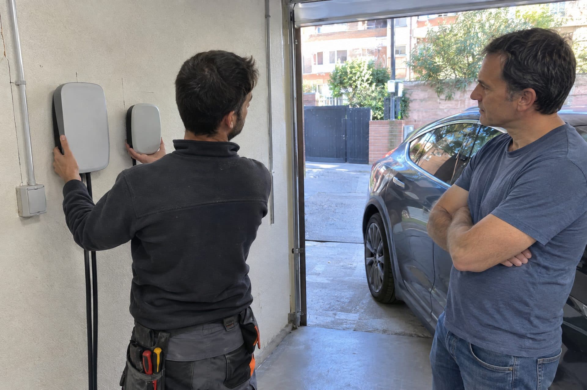 Electricista probando la posición de dos cargadores en la pared del garaje mientras el propietario lo observa