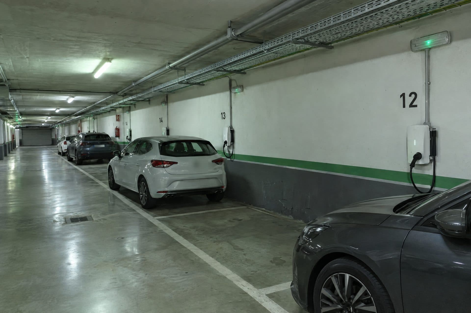 Pasillo de un garaje comunitario con bandeja por el techo y varios cargadores de pared en plazas numeradas