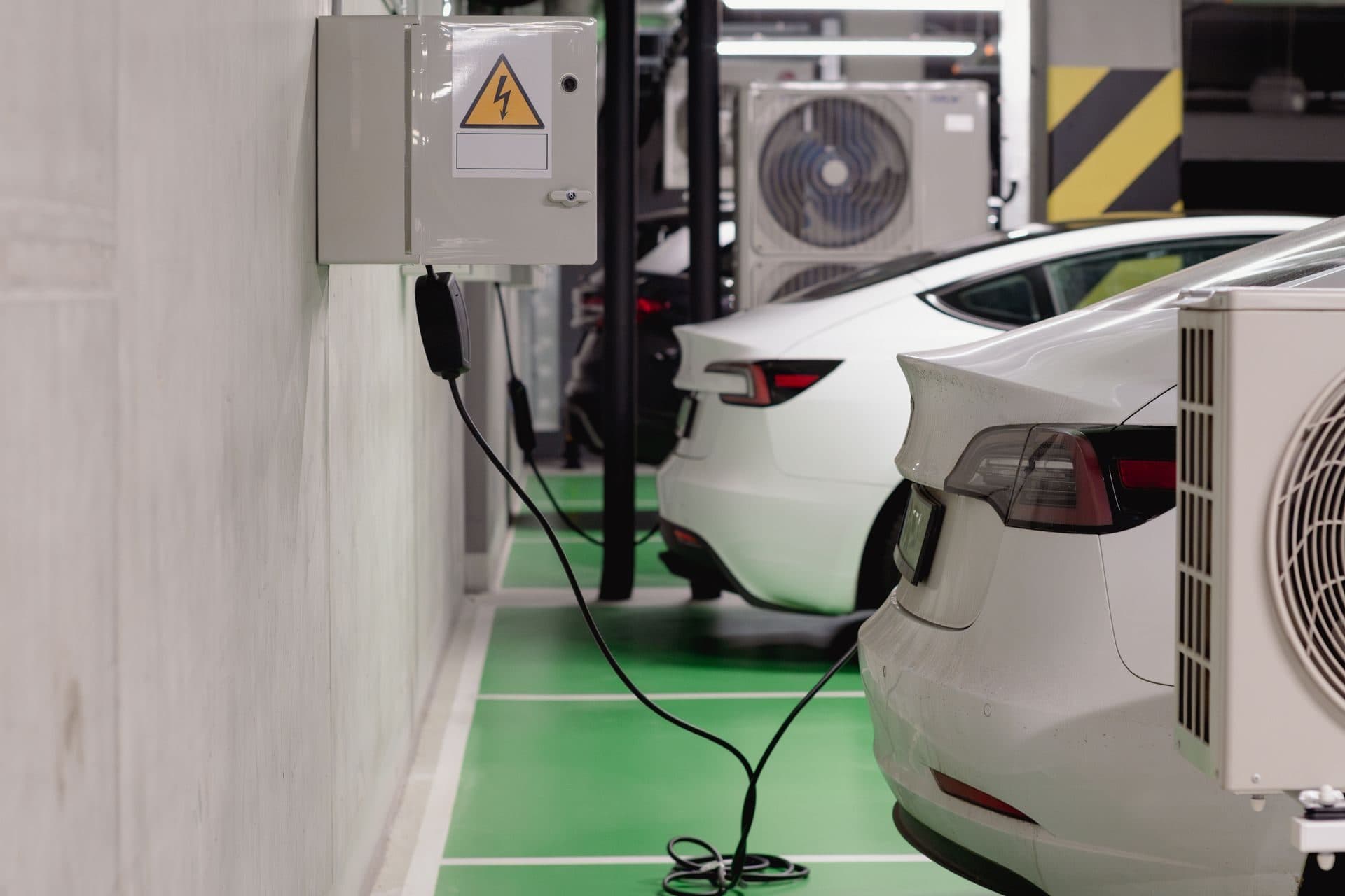 Coches eléctricos cargando en un garaje subterráneo con suelo verde y cajas de protección en la pared