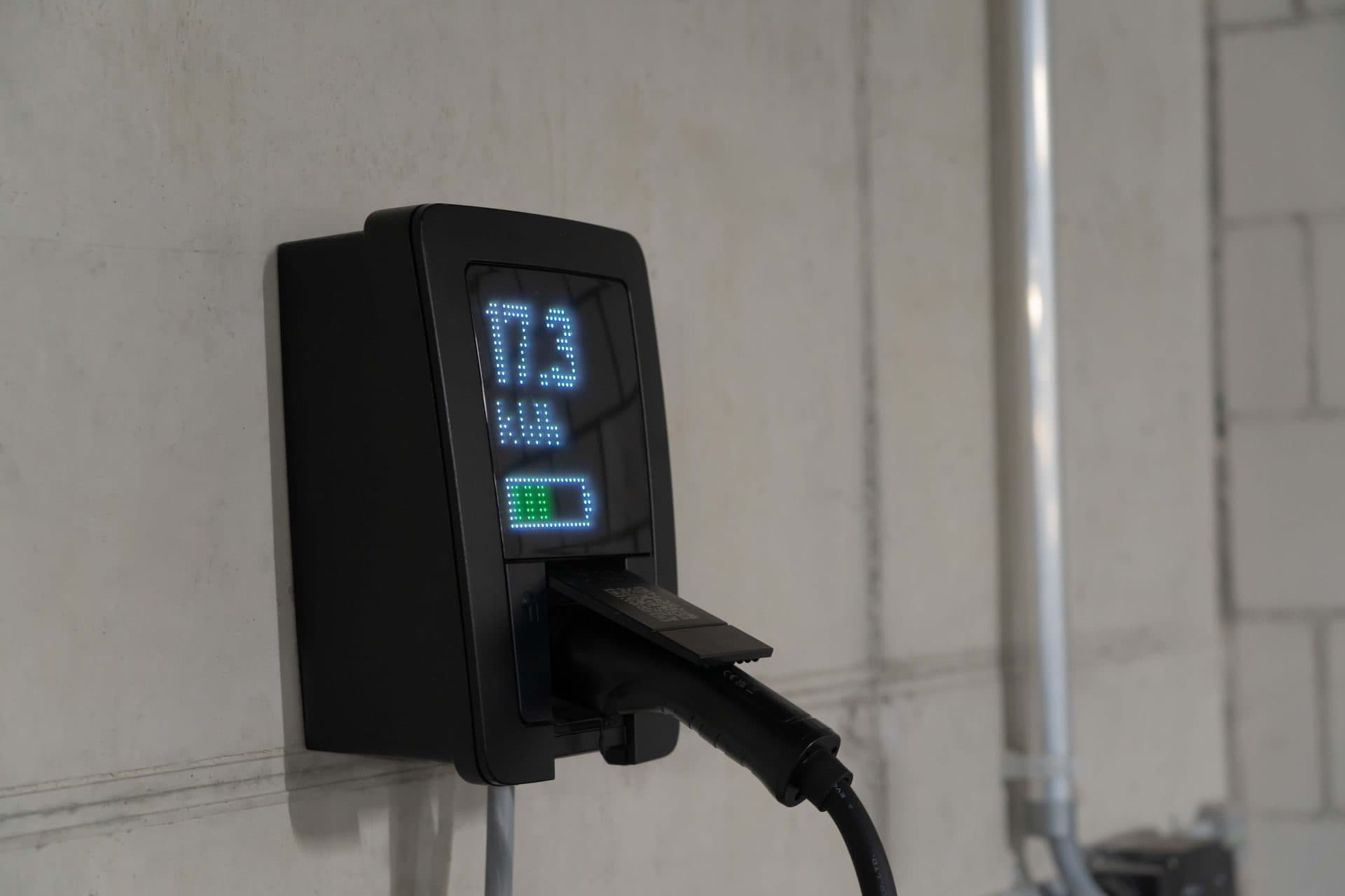 Cargador de pared con pantalla que muestra la energía cargada, en un garaje de hormigón